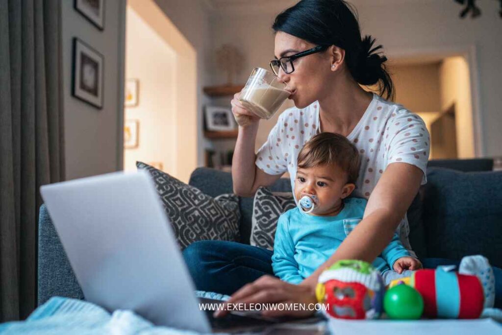 mother working on a laptop while sitting on a couch with her baby