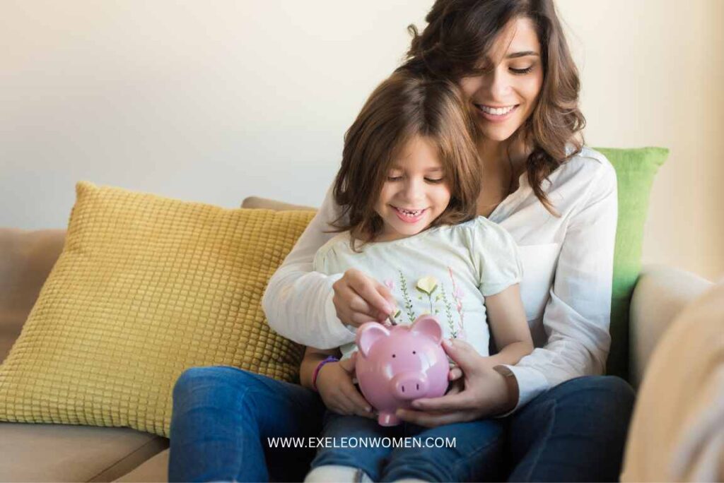 child places a coin into a pink piggy bank, with the woman guiding her hands.