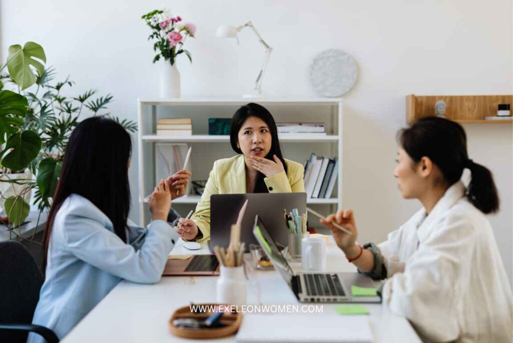 Three women sitting around a table in a bright office, engaged in a discussion.