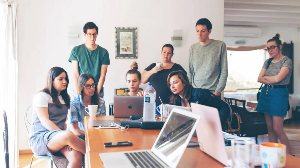 A diverse group of young professionals collaborating around a table, focused on laptops during a team meeting.
